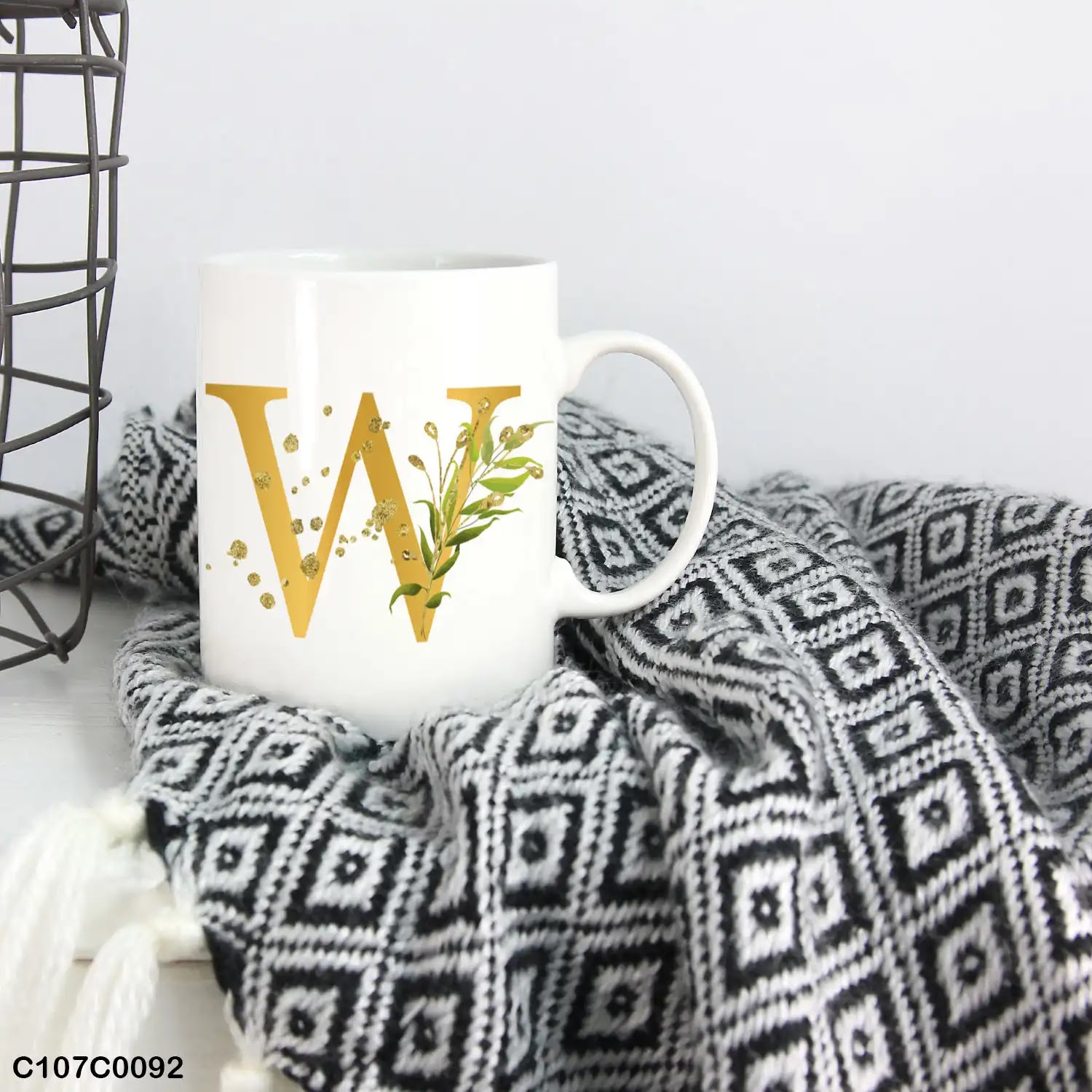 A white mug (cup) printed with gold Letter "W"and small green branch