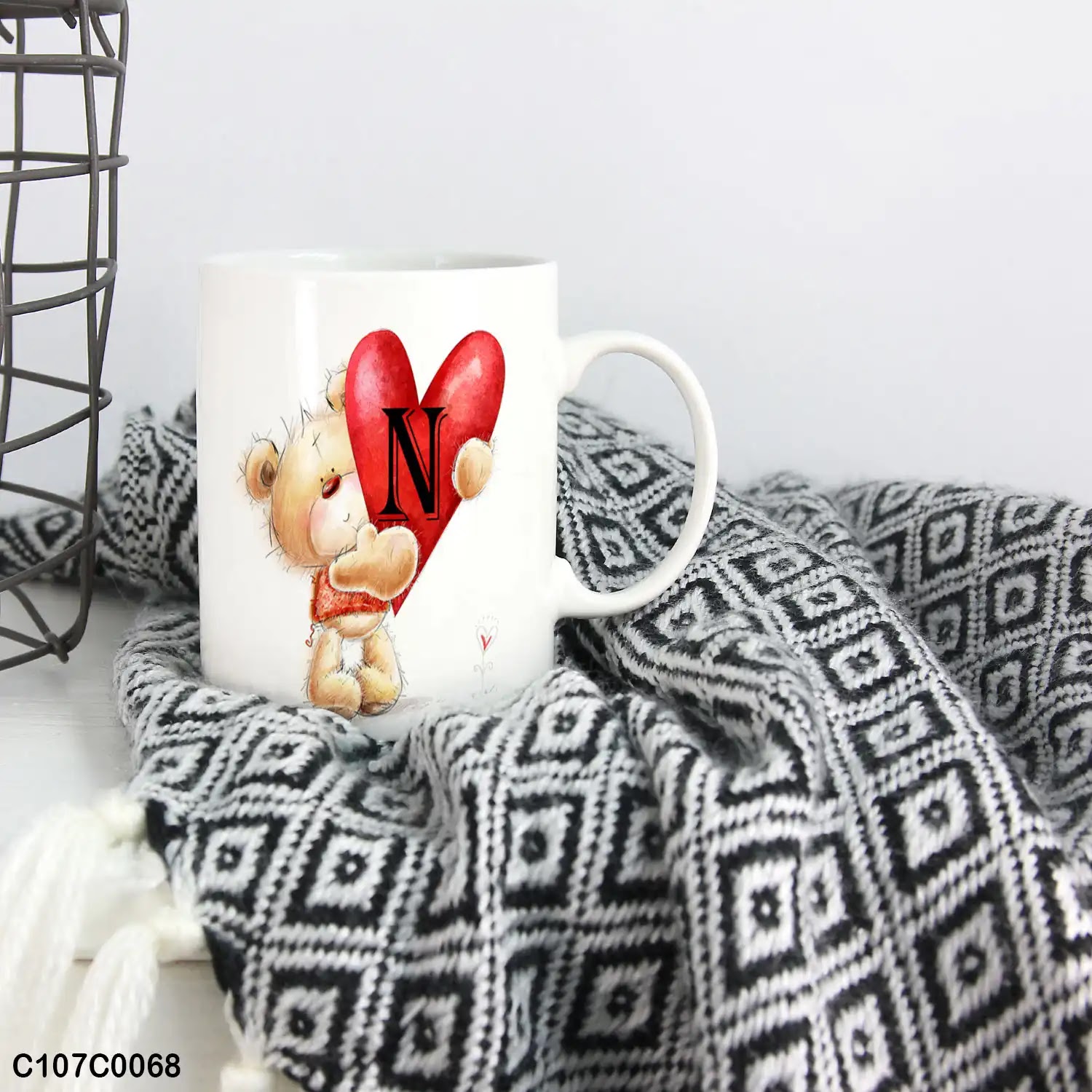 A mug (cup) printed with an image of a little bear has a heart with "N"
