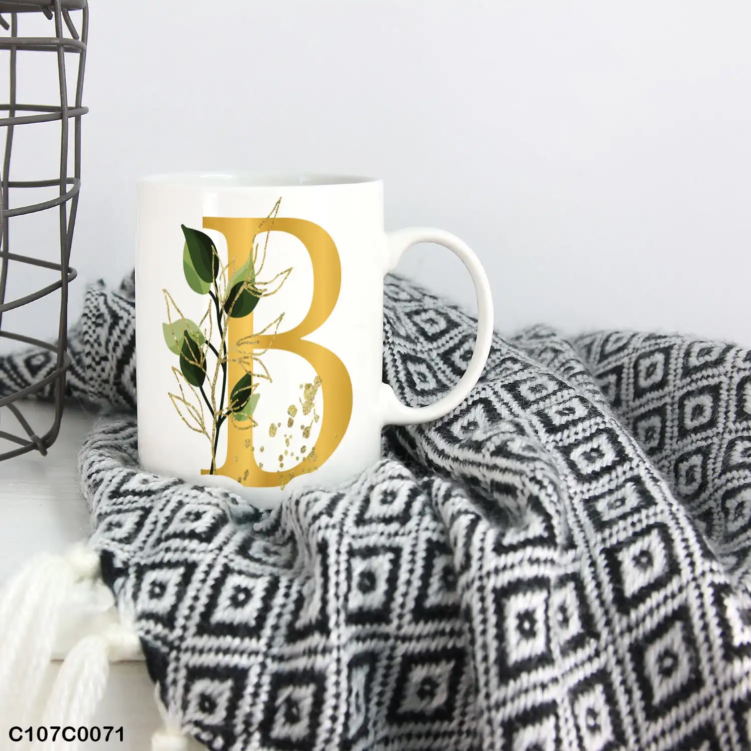 A white mug (cup) printed with gold Letter "B" and small green branch