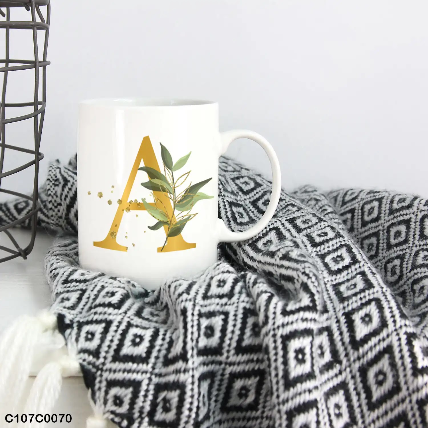 A white mug (cup) printed with gold Letter "A" and small green branch