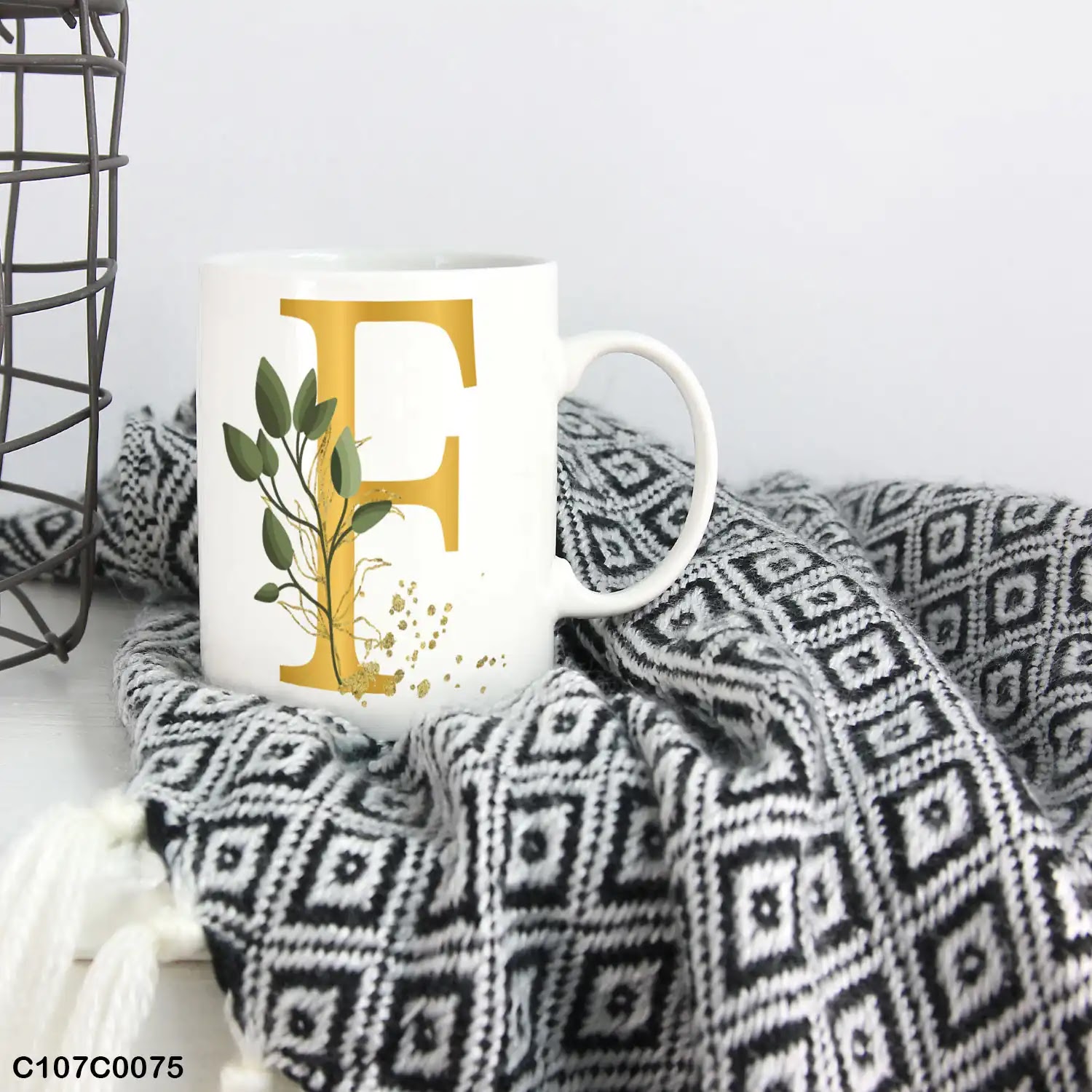 A white mug (cup) printed with gold Letter "F" and small green branch