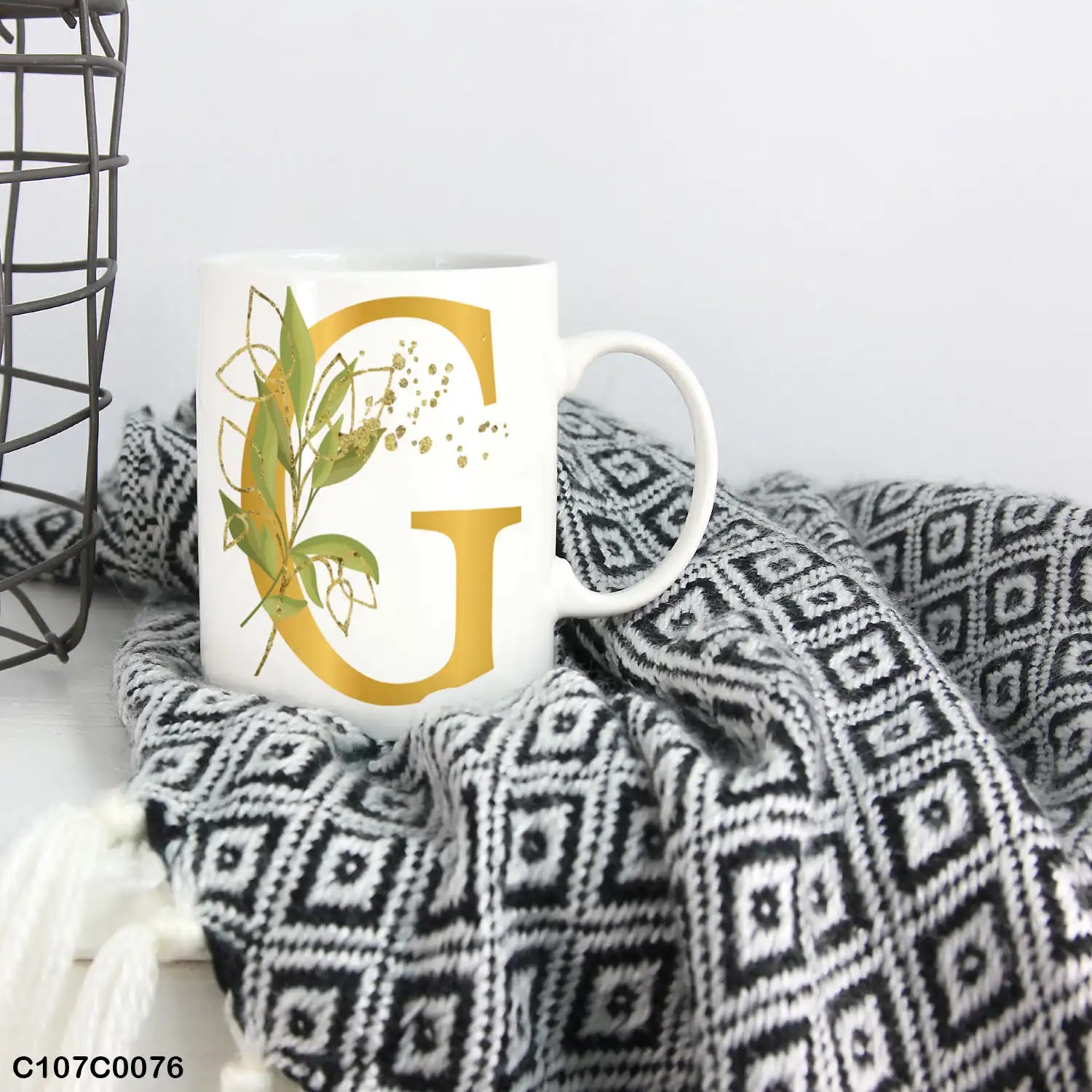 A white mug (cup) printed with gold Letter "G" and small green branch