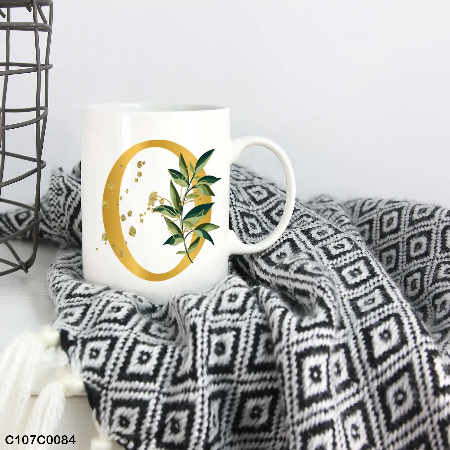 A white mug (cup) printed with gold Letter "O" and small green branch