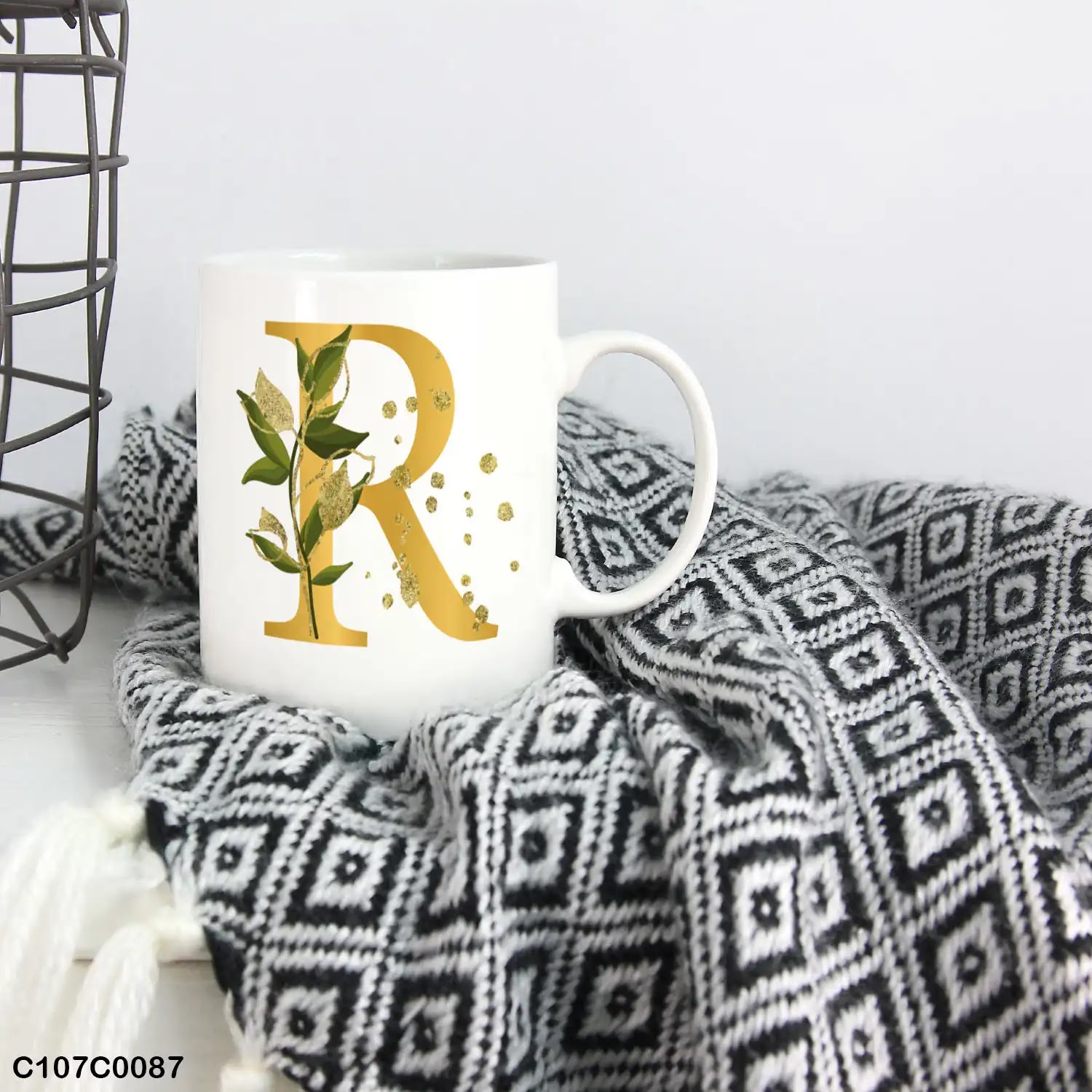 A white mug (cup) printed with gold Letter "R" and small green branch