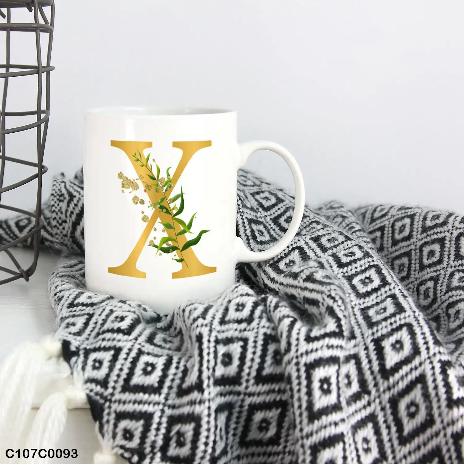 A white mug (cup) printed with gold Letter "X"and small green branch