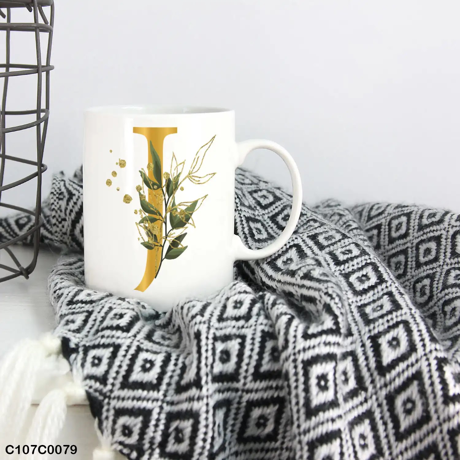A white mug (cup) printed with gold Letter "J" and small green branch