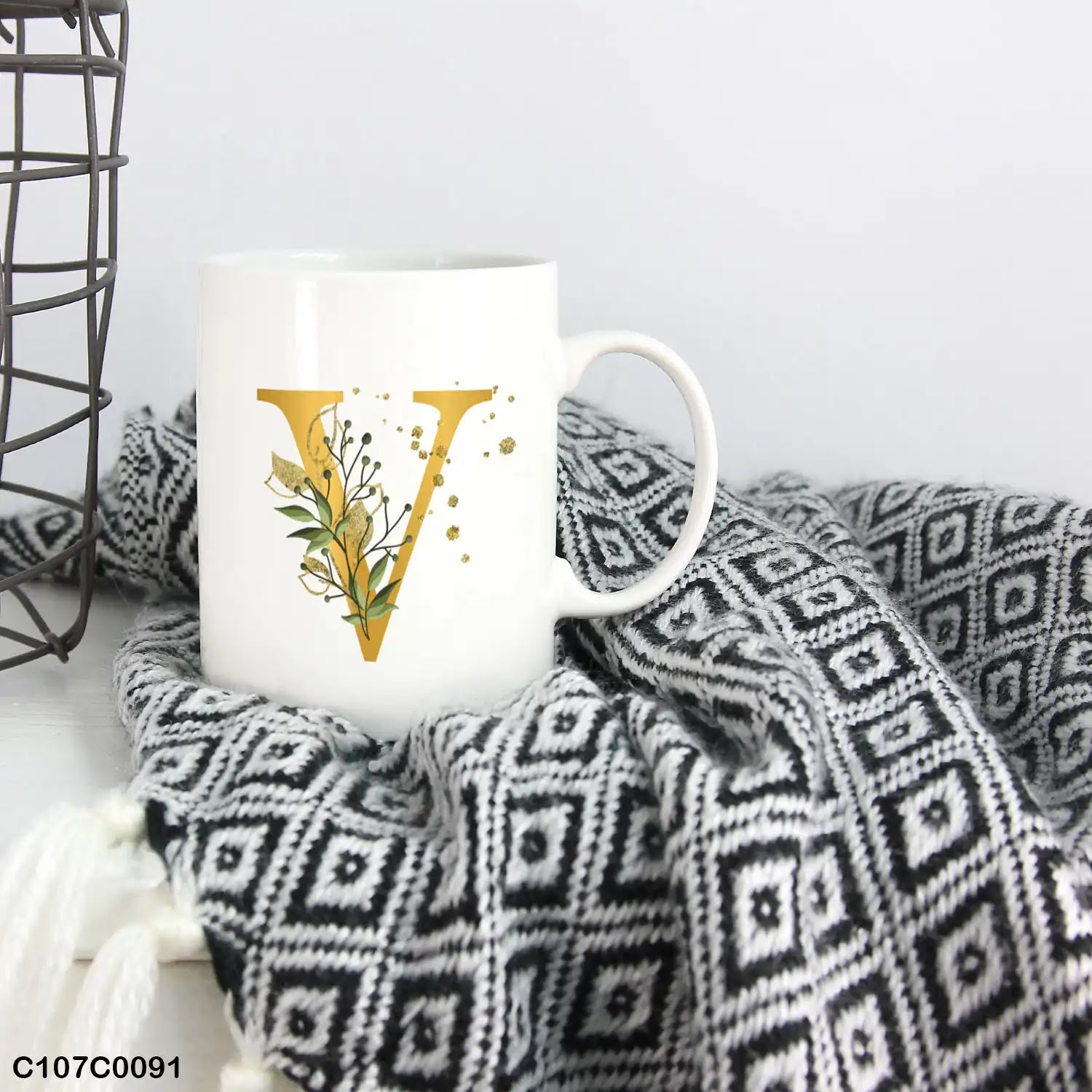 A white mug (cup) printed with gold Letter "V"and small green branch