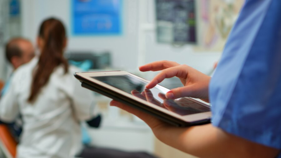 Nurse using a tablet in a dental clinic while the doctor treats a patient.