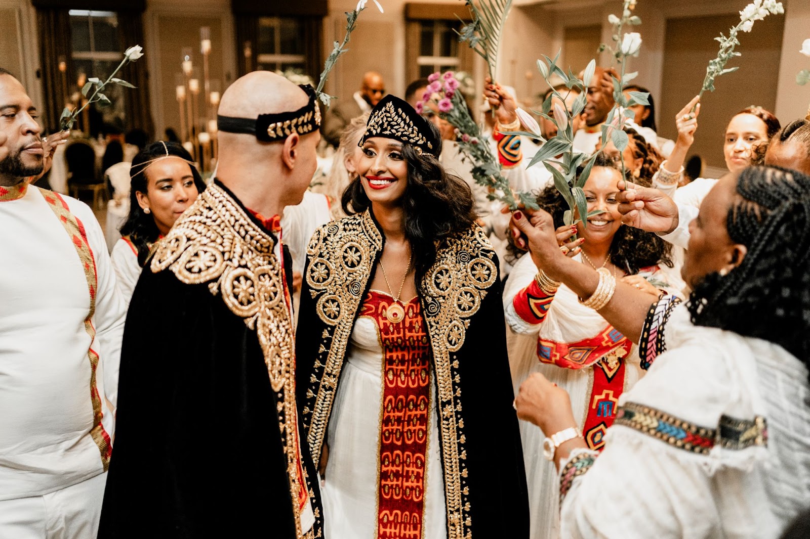 Bride and groom in Eritrean attire, guests holding palms and roses in the air