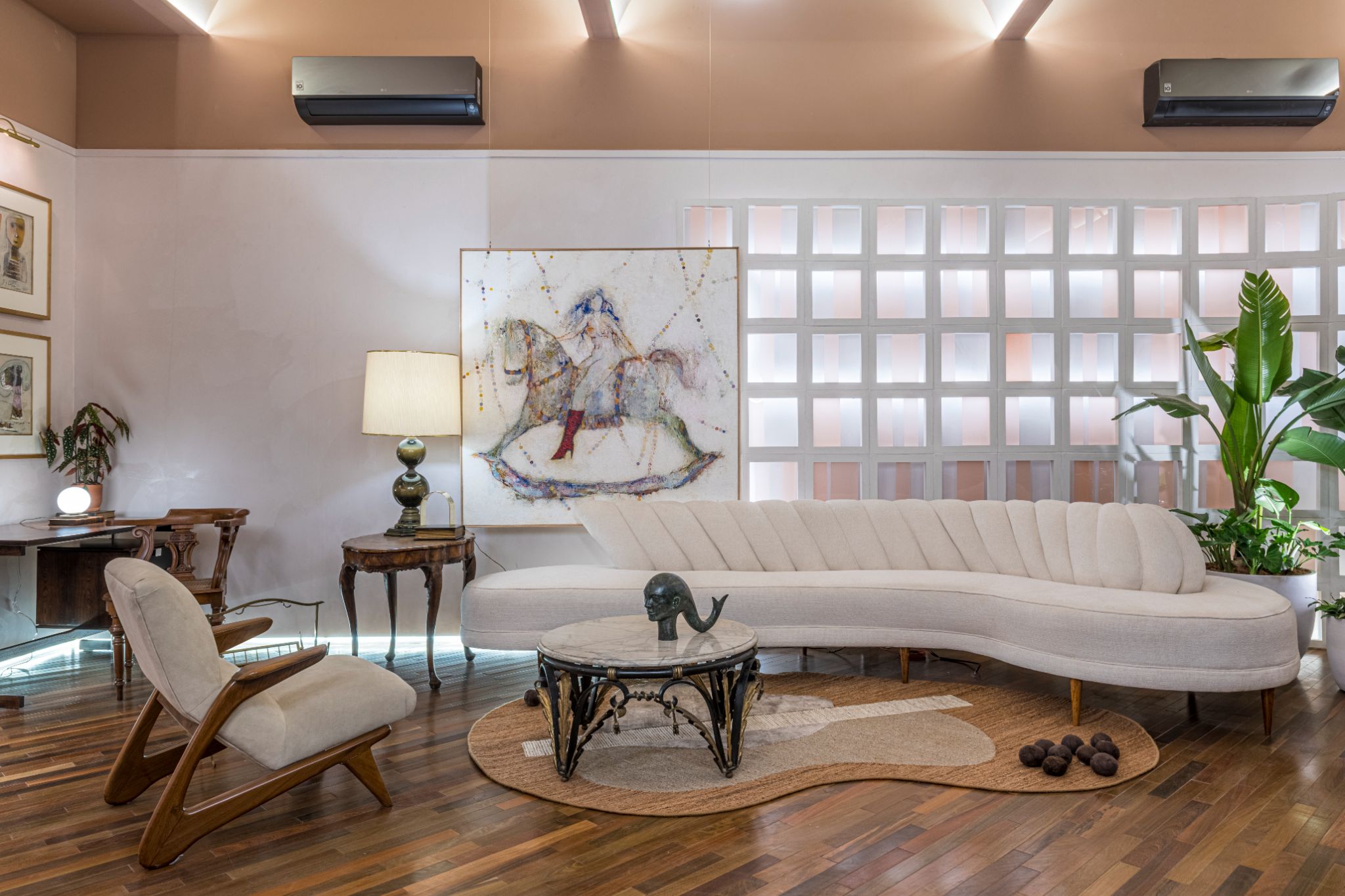 Sala com piso de madeira, sofá e paredes brancas com cobogó branco e vasos de plantas.