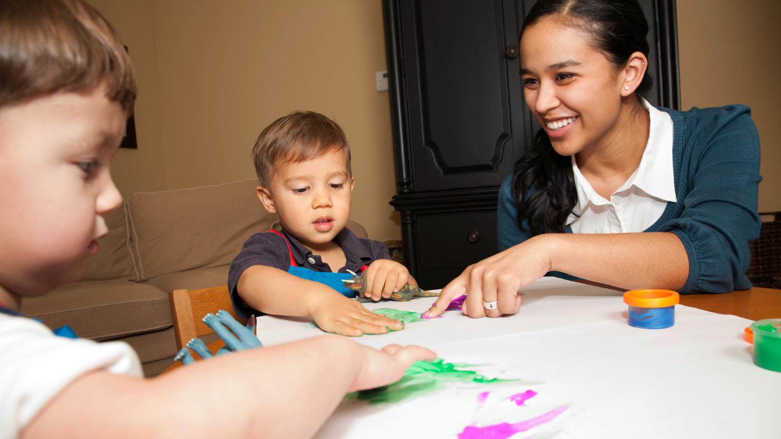 childcare worker showing two children how to fingerpaint