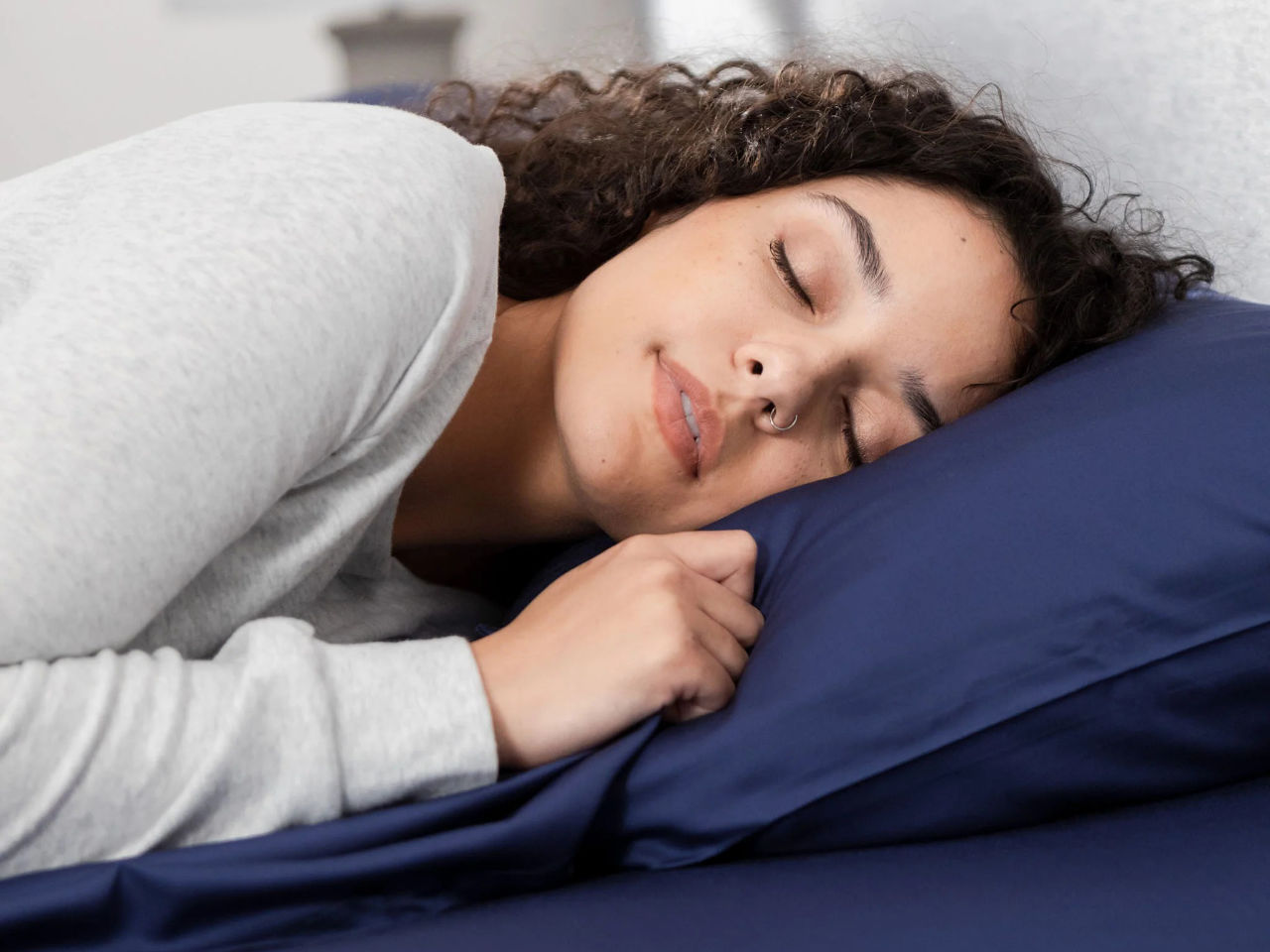 A woman sleeps soundly on navy blue Hush sheets.