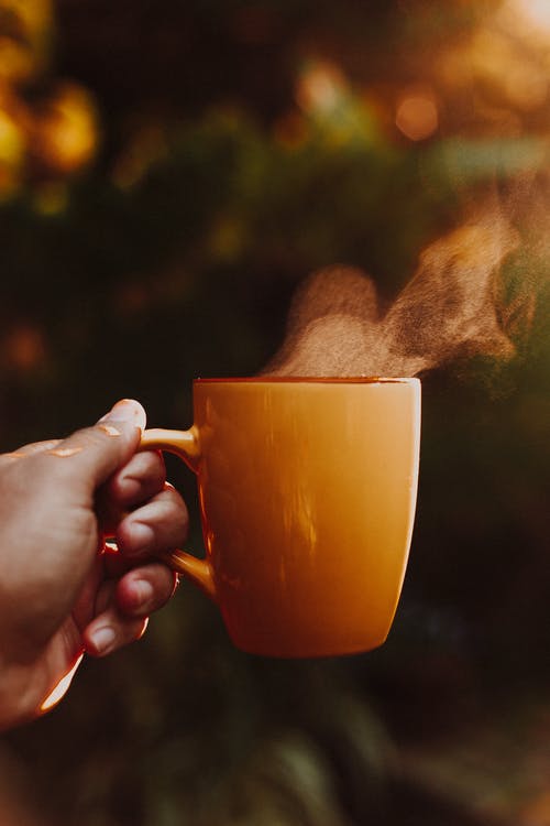 Photo of a Hand Holding Out a Steaming Cup