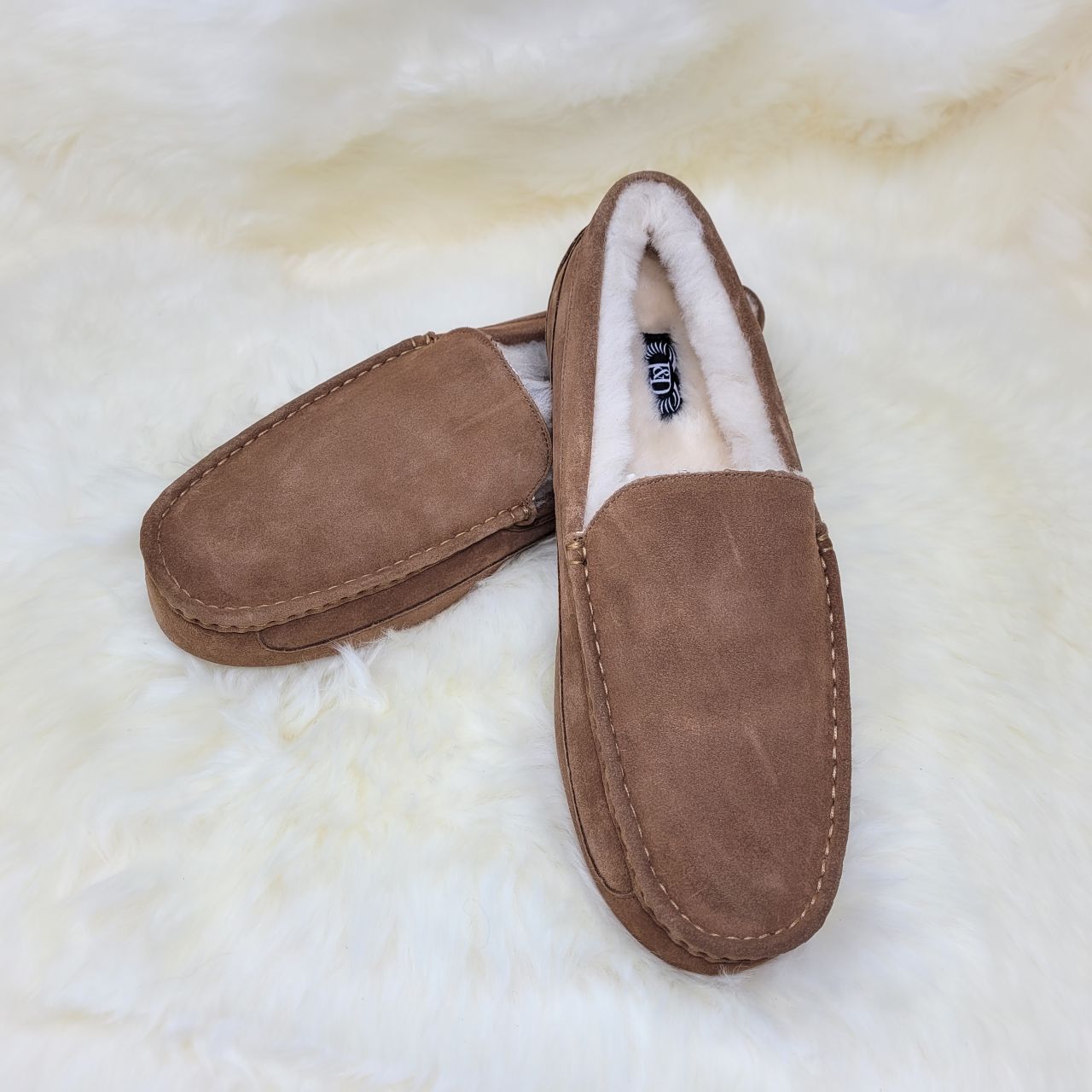 Men's chestnut moccasin slippers sat on a white sheepskin rug