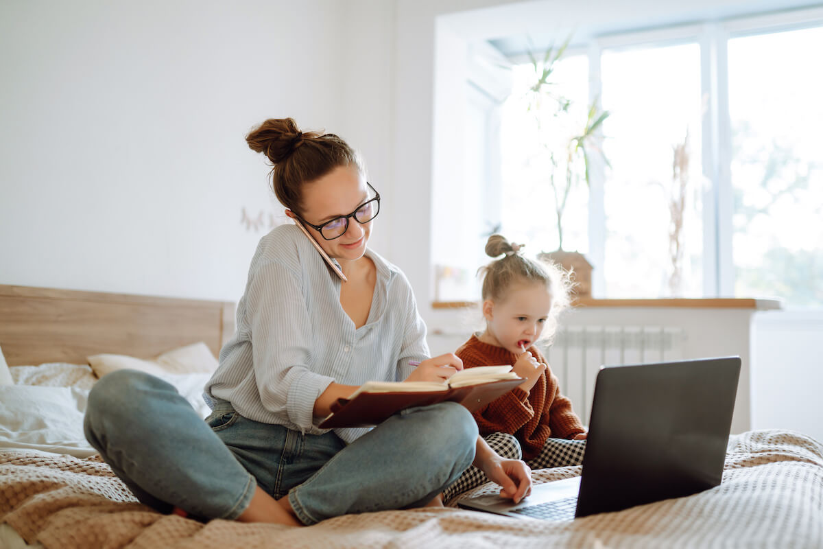 Mom working at home while her toddler sits beside her