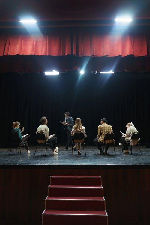 3 women and 3 men on stage reading their script 
