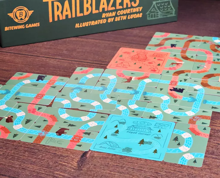 Sidelong view of Trailblazers boardgame with tiles in forground and bottom of box cover in background