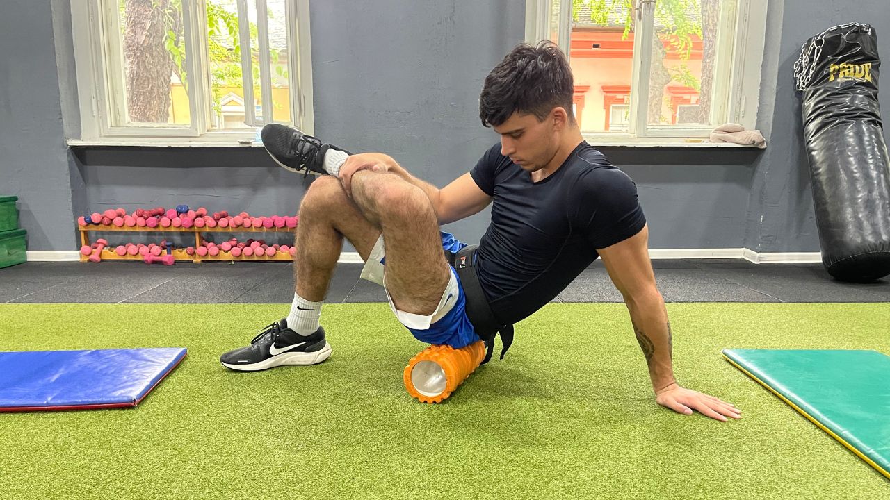 Vanja performs a seated foam roll exercise for the lower back in the commercial gym setup.