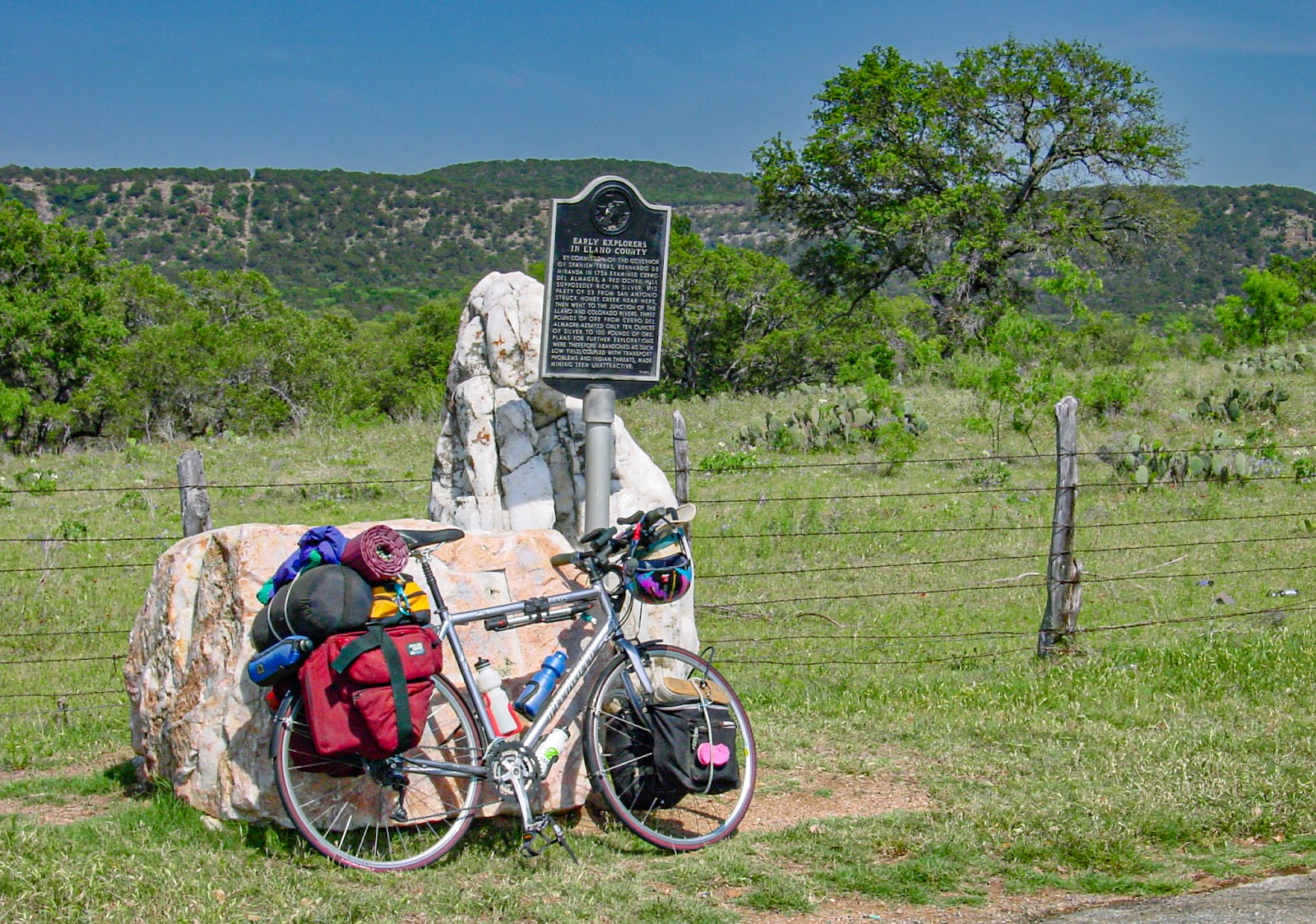 Bike leaning on rocks that surround an Interpretive sign on the side of a road. Hills in the background. 