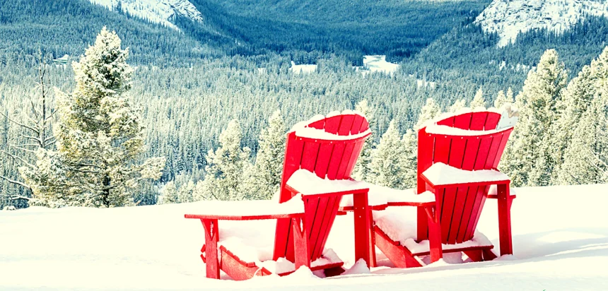 Two red Adirondack chairs in a snowy landscape.