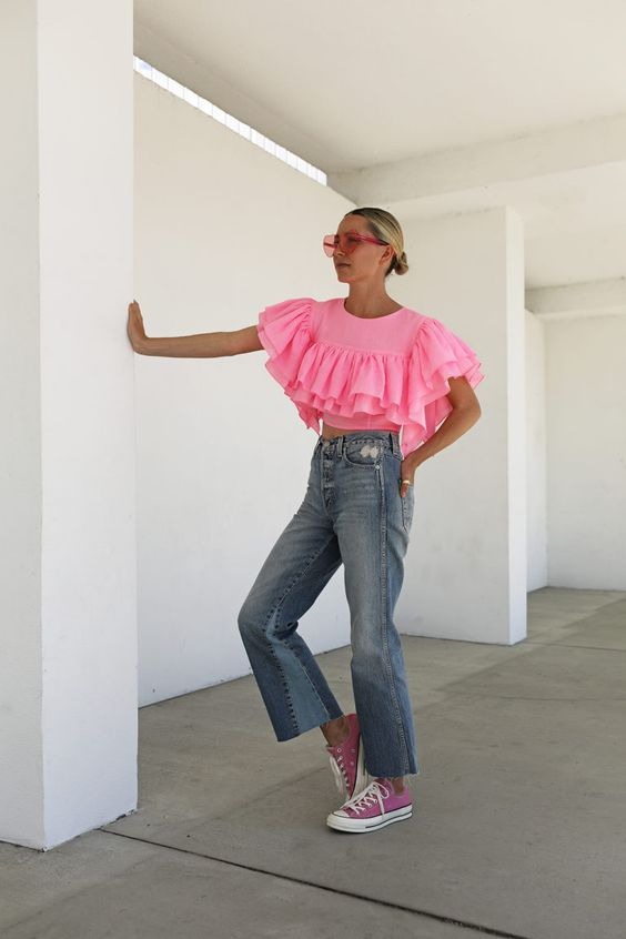 A lady wearing a pink, top, jeans, and pink sneakers