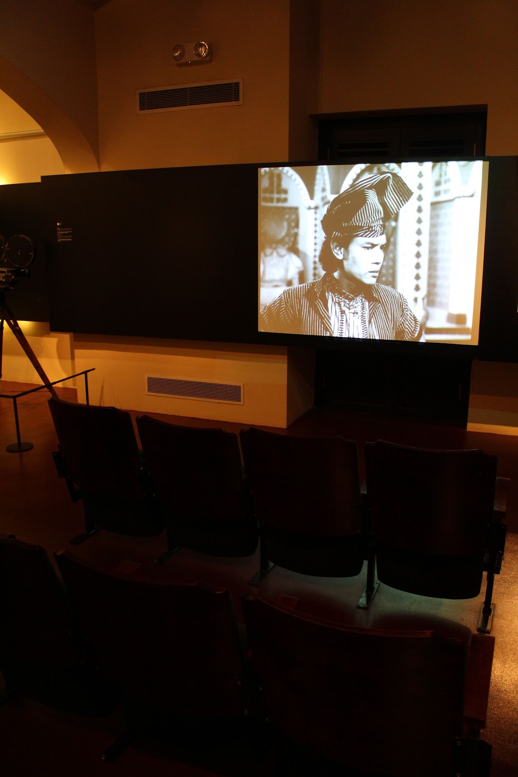 Seating facing a black and white screen, playing an old Malay film