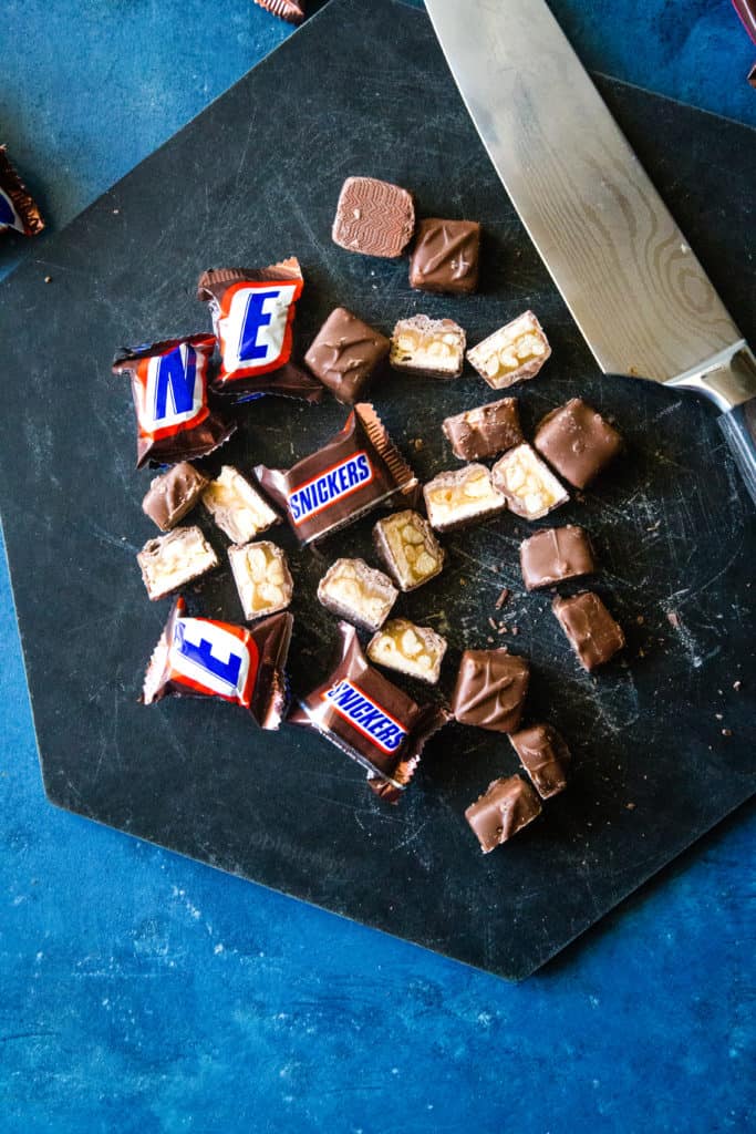 Black cutting board with snickers minis cut in half and knife to the side. 