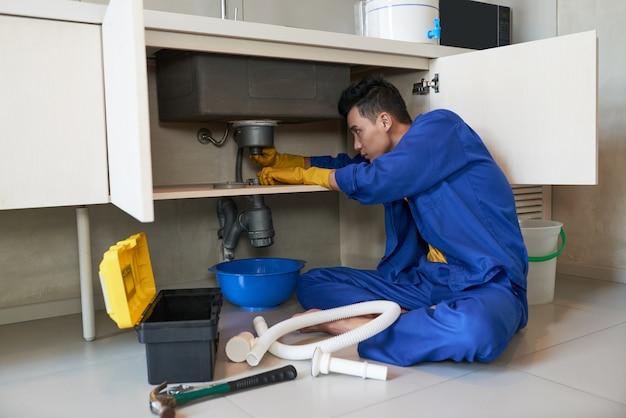 Encanador asiático de macacão azul, limpando o bloqueio no ralo de Assistência Flex Domiciliar