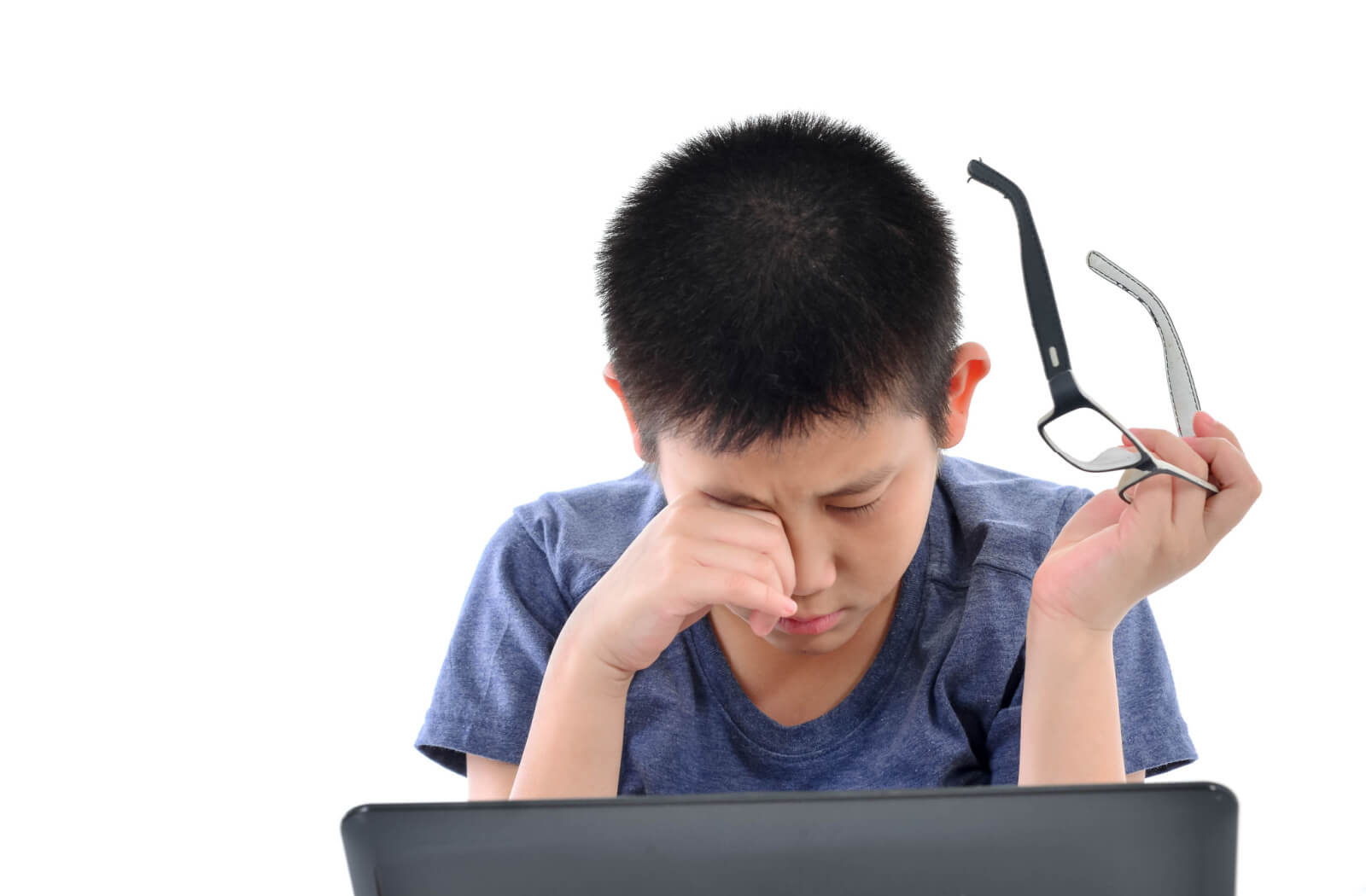 A boy scratching his right eye, experiencing blurry vision while sitting in front of his computer.