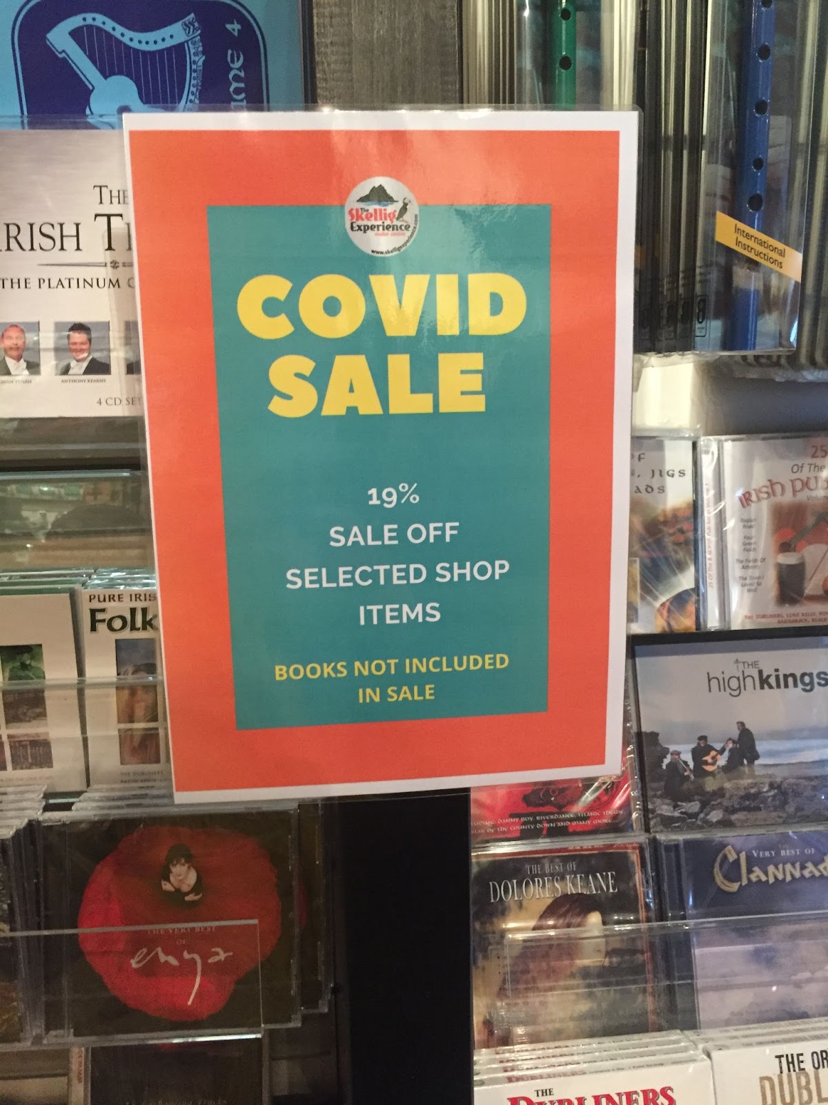 A sign with a thick red border and teal background reads "COVID SALE: 19% sale off selected shop items. Books not included in sale." 