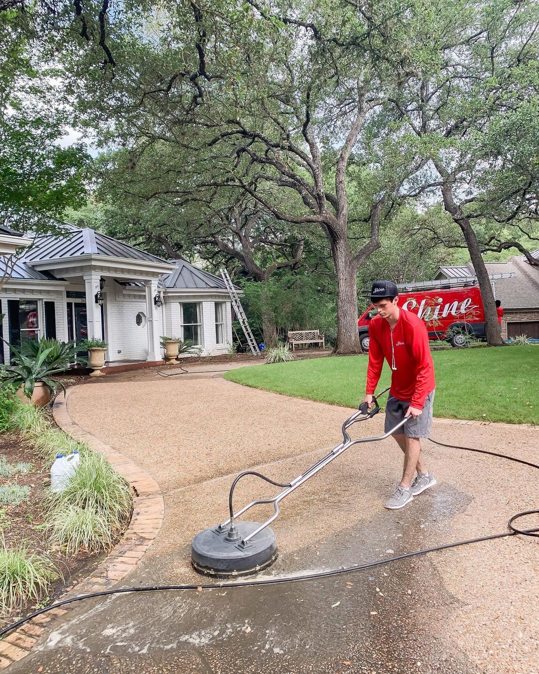 A Shine employee washing someone’s front driveway with a Shine van in the background.