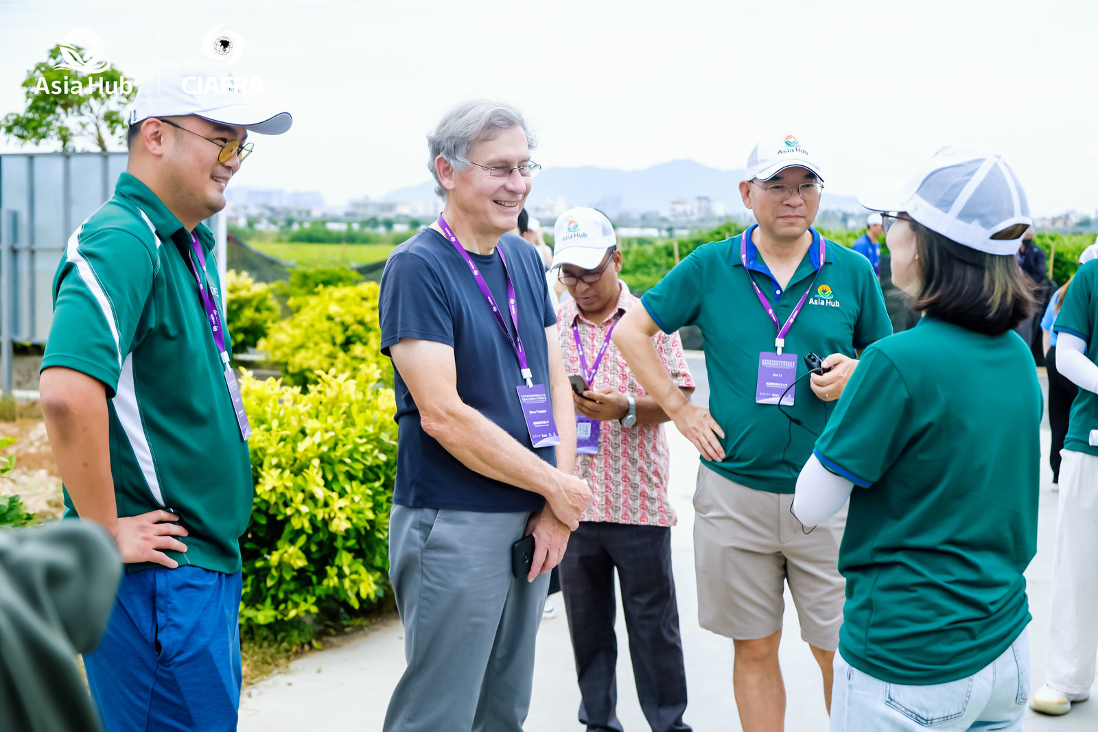 a small group of people smile standing in a path that goes through a field, seemingly in conversation