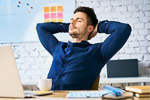 Businessman relaxing at work with hands behind head, eyes closed and a coffee. No tinnitus symptoms present.