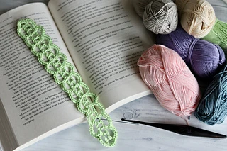 green lace bookmark on open book with yarn skeins