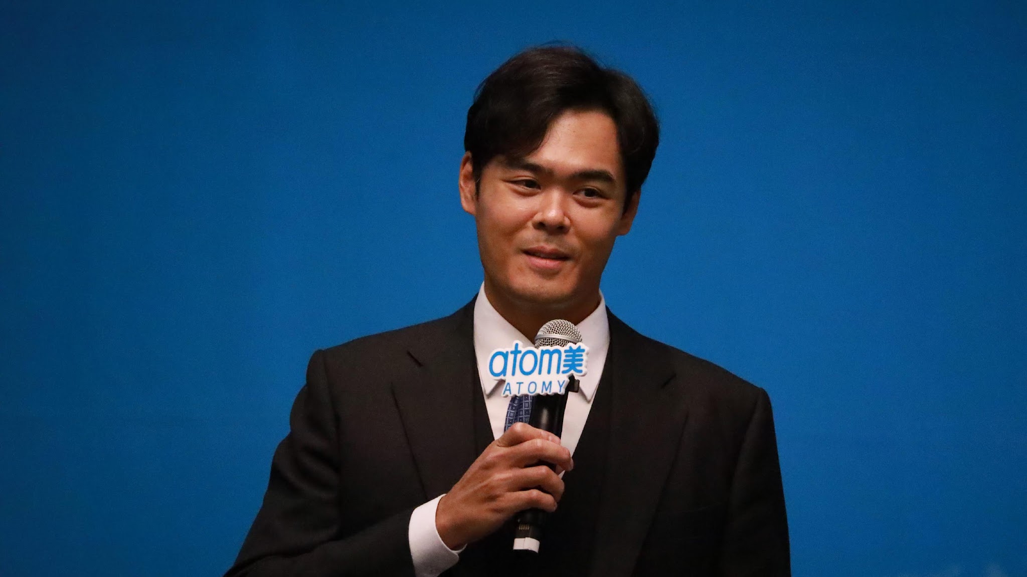 A person in a suit holding a microphone

Description automatically generated