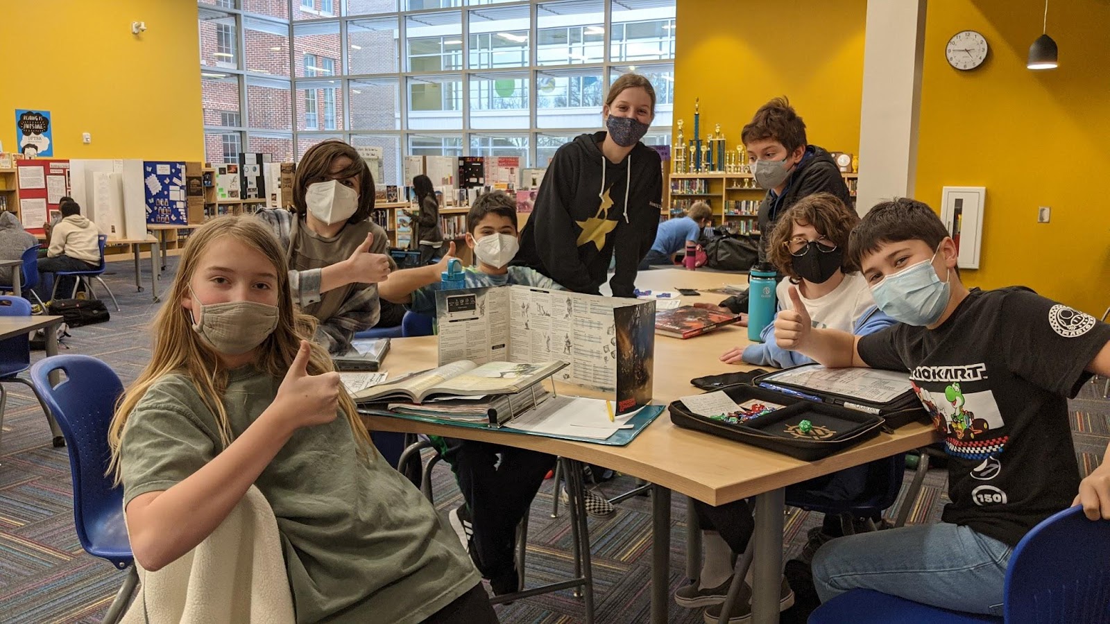 masked middle school aged students at a table engaged in gameplay in the library