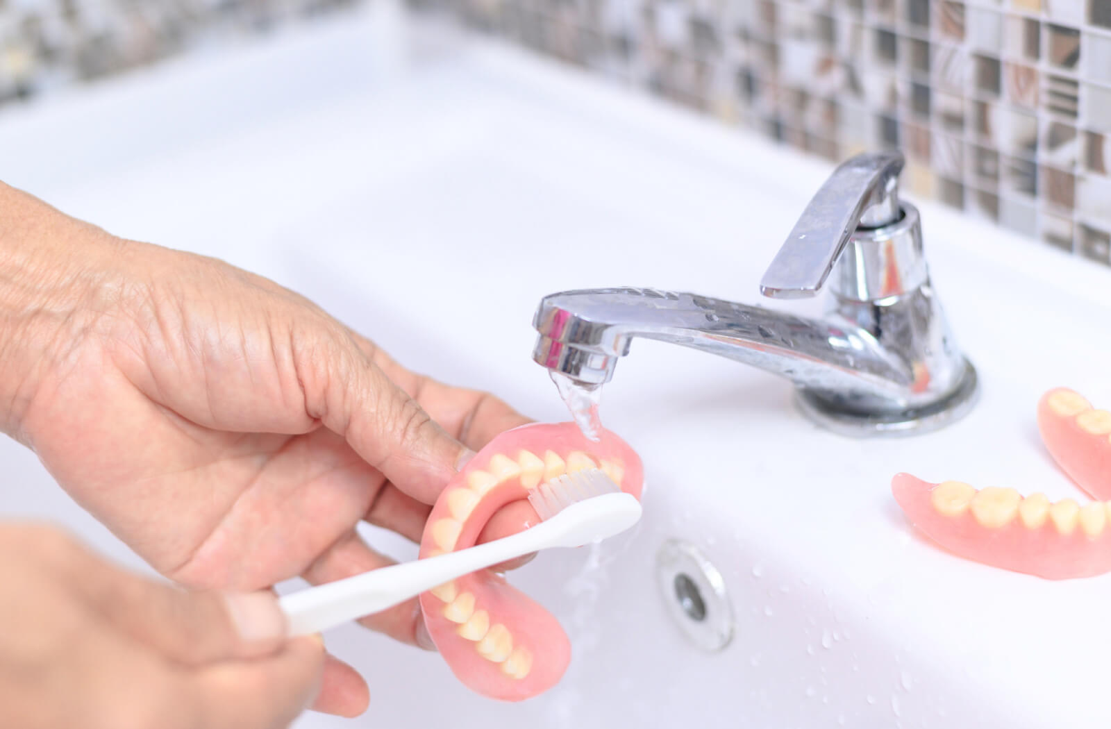 A close-up of senior person's hands using a soft-bristle brush to clean their dentures.