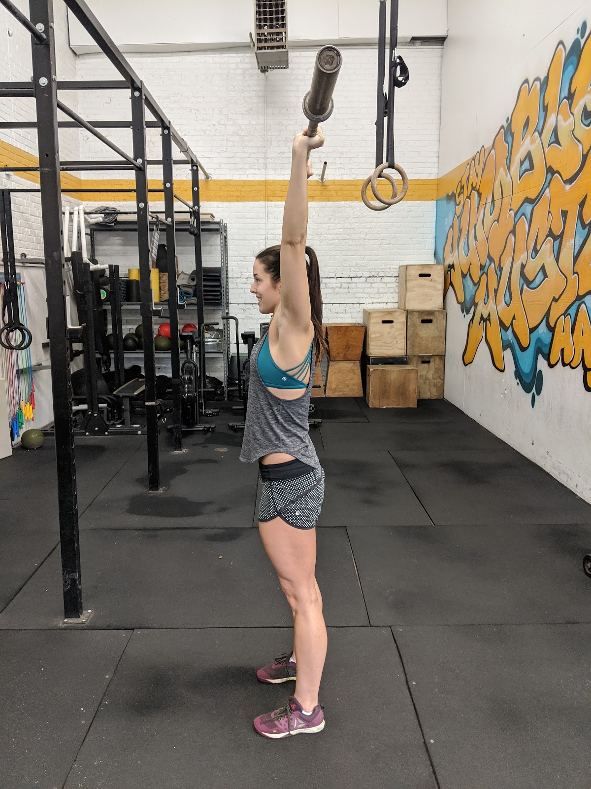 side view of woman standing with empty barbell overhead
