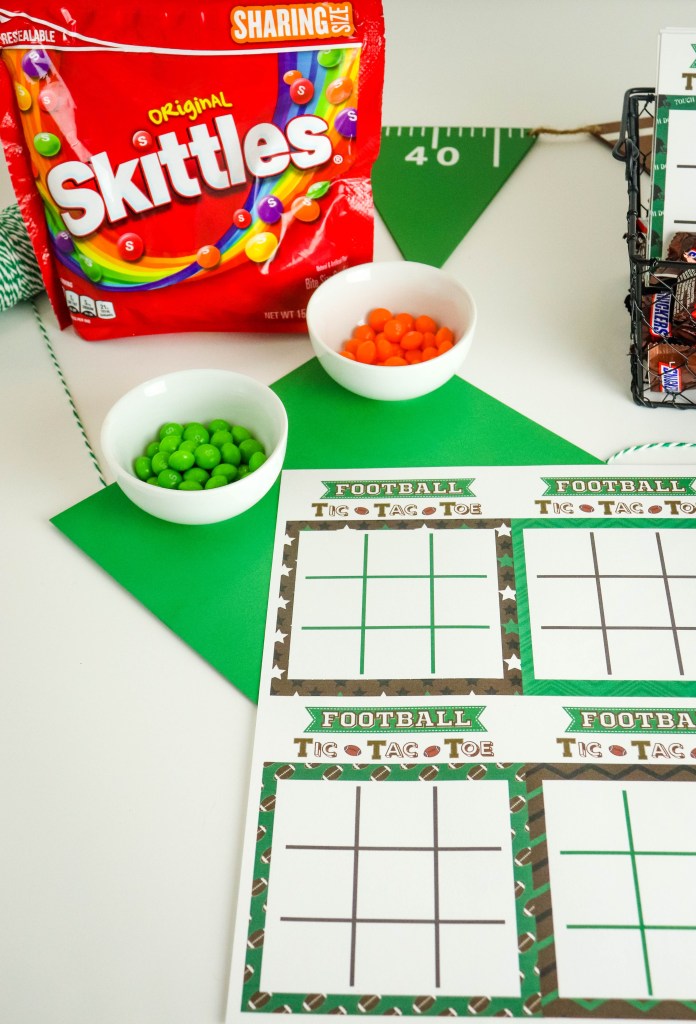 Football Tic Tac Toe sheets on green paper with bowls of green and orange skittles, a package of skittles and football banner 