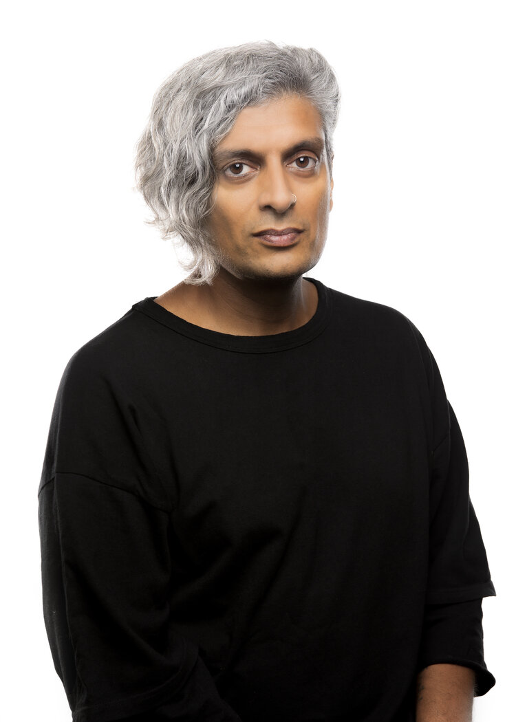 Image description: Indian man with wavy, salt-and-pepper hair and a nose ring wearing a black shirt.