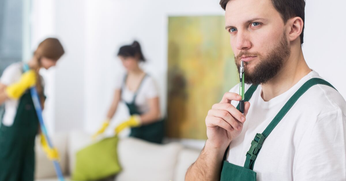 Young man with beard contemplating while two women clean in background