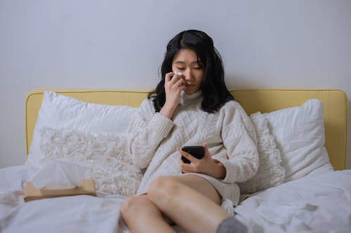 Free A Sad Woman Looking at her Cellphone While Sitting on a Bed Stock Photo