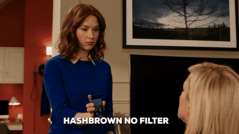 The character, Kimmy Schmidt, from the show UNBREAKABLE KIMMY SCHMIDT, holding up her smartphone and saying the phrase "Hashbrown no filter."