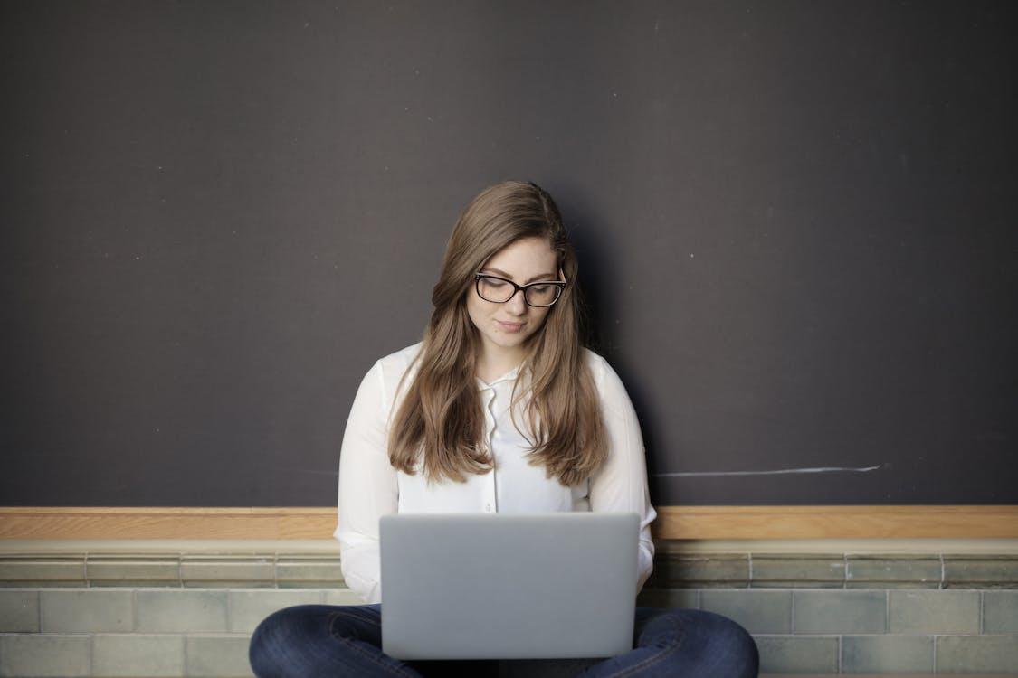 Free Woman in White Long Sleeve Shirt and Blue Denim Jeans While Using Macbook Stock Photo