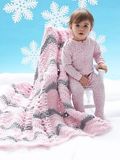 toddler sitting on chair that has a super bulky crochet baby blanket draped on the chair