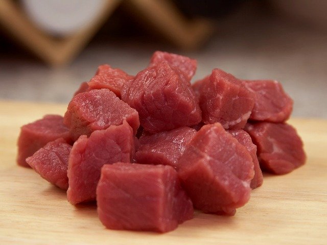 A small pile of cubes of raw meat on a cutting board.