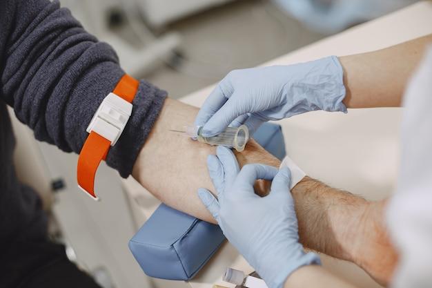 Enfermeira hábil está fazendo exame de sangue para um homem na clínica como um dos benefícios da assistência médica ambulatorial básica coletiva