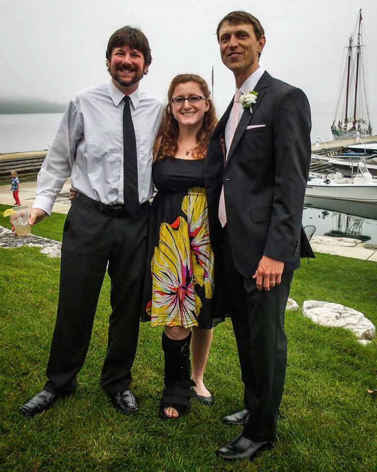 3 white people dressed for a wedding against a boat dock background