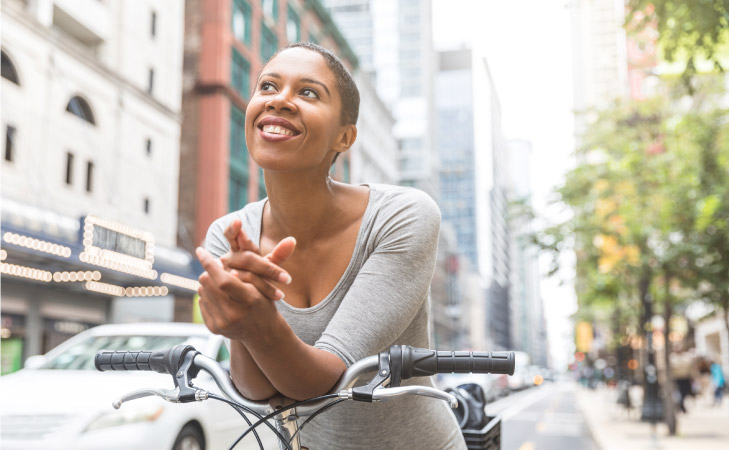 A happy young woman leaning on her bicycle handles while waiting at a stop light in Chicago. She is smiling and looking out, thinking about something pleasant.