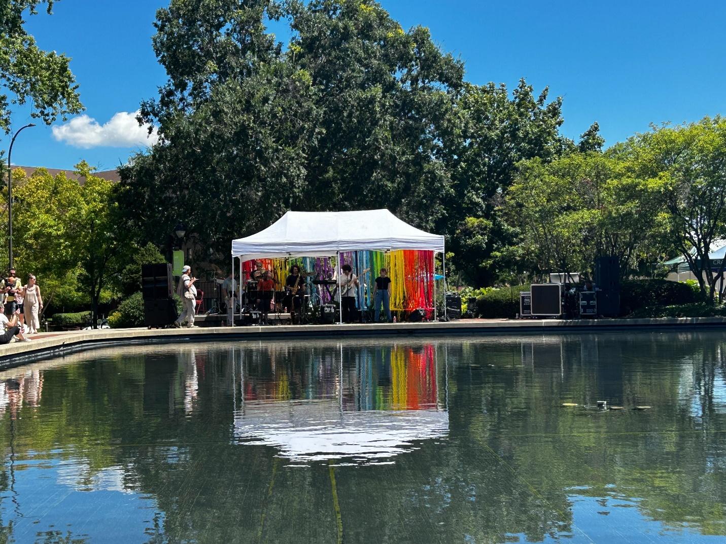 A white tent with colorful cloths on the side of a pond

Description automatically generated